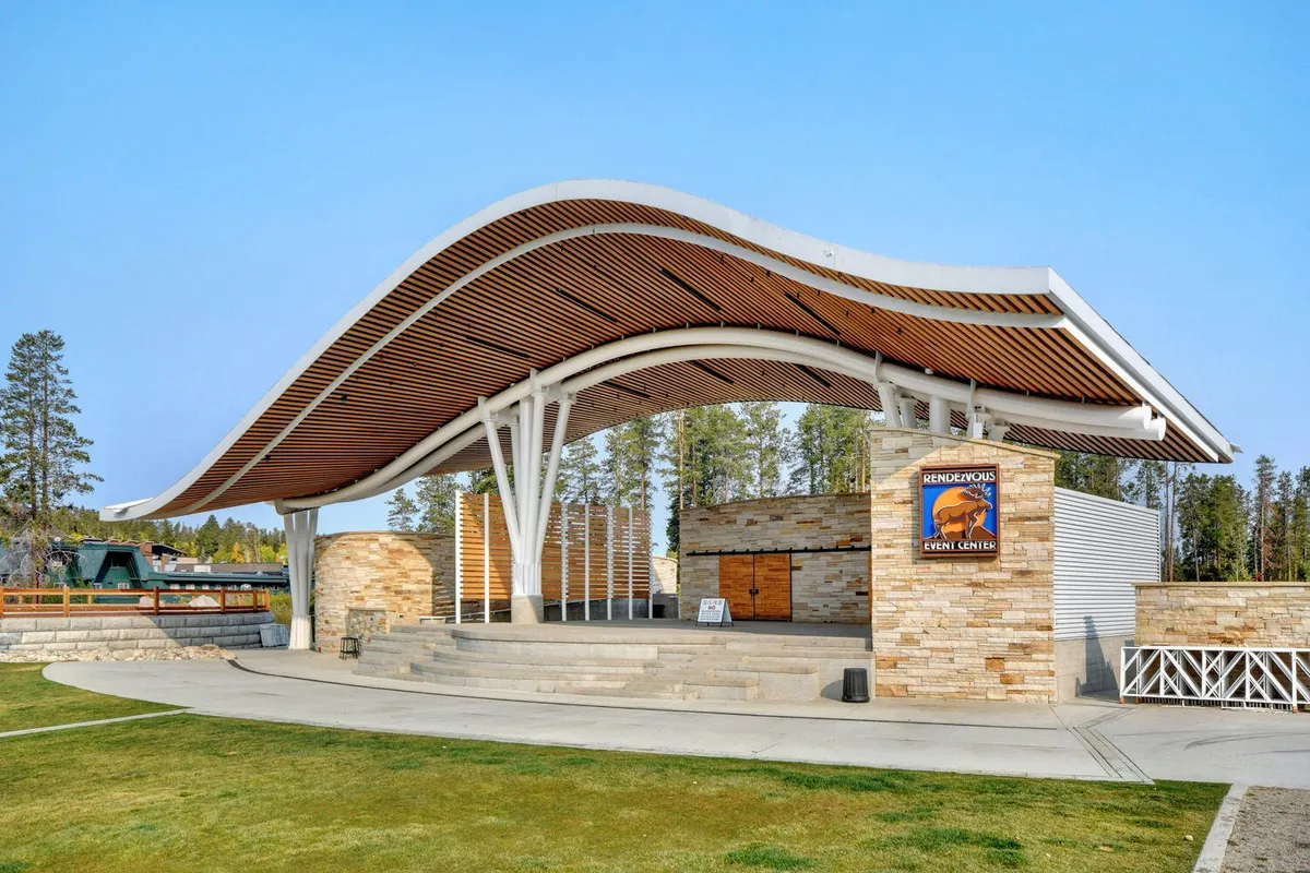 An inviting outdoor venue featuring a curved roof structure, stone walls, and wooden accents—ideal for concerts, community events, and family gatherings.