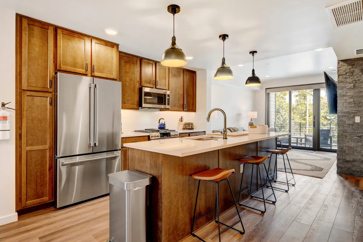 The image showcases a stylish, sunlit kitchen with a spacious central island featuring comfortable seating, modern stainless steel appliances, and expansive windows that fill the space with natural light. The setting is ideal for cooking, entertaining, and gathering, with an inviting atmosphere that encourages guests to share meals and create lasting memories together.
