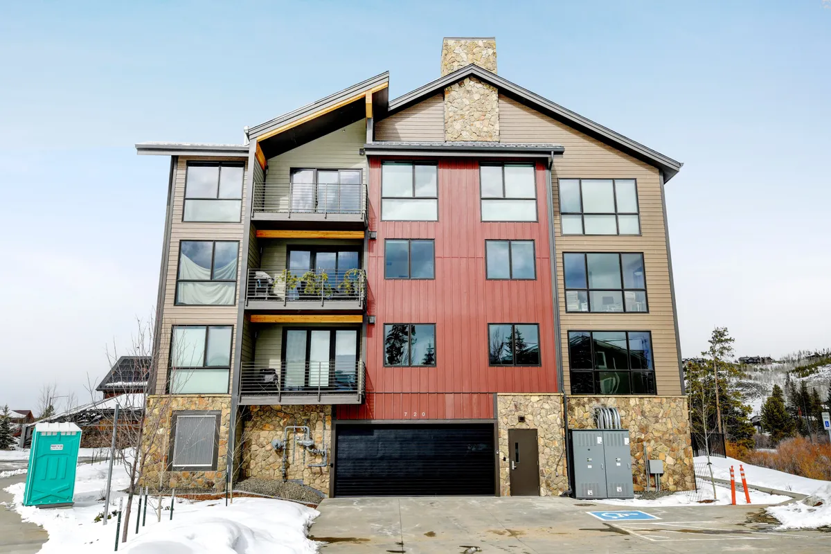 A modern condo exterior with striking architecture, large windows, and colorful siding, capturing a lively, welcoming atmosphere. The balconies hint at social gatherings and the vibrant community just steps away from local attractions like Hideaway Park Amphitheater.