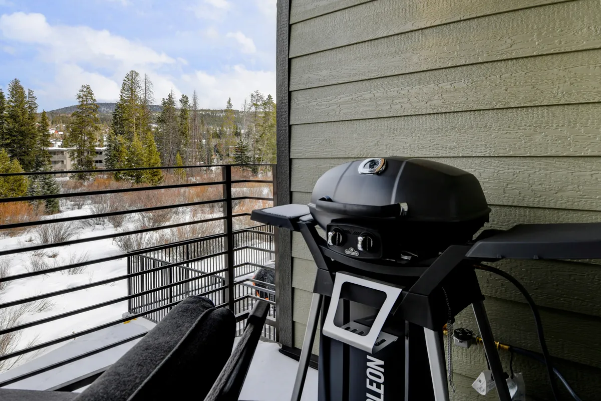 An inviting exterior balcony area featuring a grill, comfortable seating, a railing, and a panoramic mountain view. The space is ideal for outdoor relaxation, barbecues, and gathering with friends while enjoying scenic surroundings.