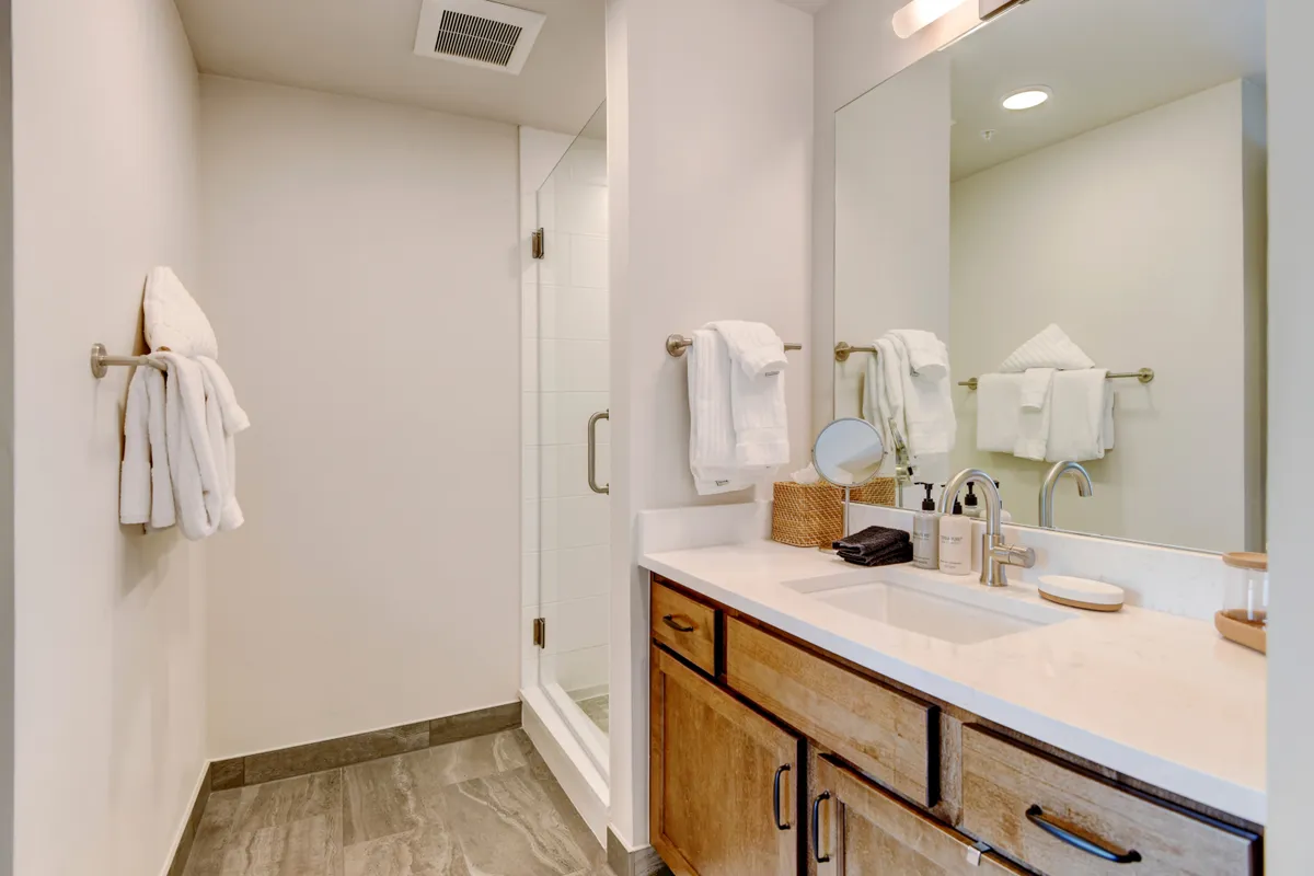 A contemporary bathroom with a vanity and sink, large mirror, shower area, and neatly arranged towels. The atmosphere is spa-like and rejuvenating, suggesting both comfort and luxury.