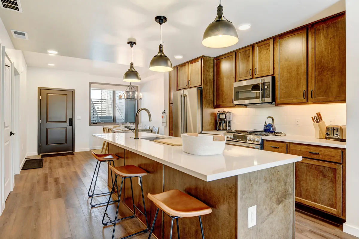 A beautifully appointed kitchen featuring a spacious island with bar seating, pendant lights, sleek stainless steel appliances, and elegant wooden cabinets. The scene exudes an inviting atmosphere, suggesting a space perfect for cooking, entertaining, and family gatherings.